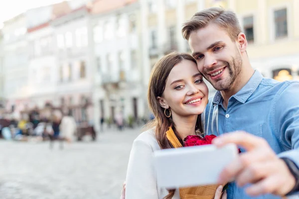 Selective focus of smiling tourists taking selfie with smartphone on street — Stock Photo