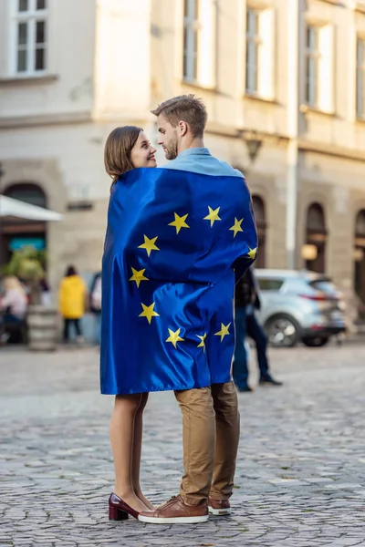 Turistas felices, envueltos en la bandera de la unión europea, mirándose unos a otros en la calle - foto de stock