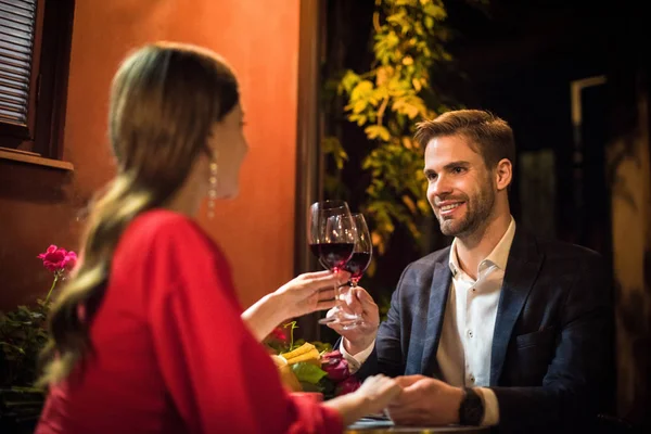 Feliz hombre tintineo vasos de vino tinto con novia mientras que hacer propuesta de matrimonio - foto de stock