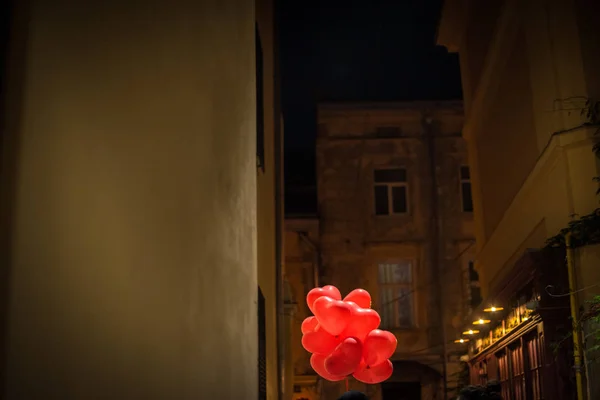 Bundle of red heart-shaped festive balloons on night street — Stock Photo