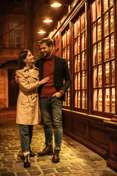 Glückliches Mädchen, das den hübschen Freund ansieht, der nachts in der Nähe des Schaufensters steht — Stockfoto