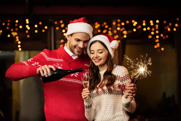 Alegre hombre verter champán en vaso de feliz novia celebración sparkler - foto de stock