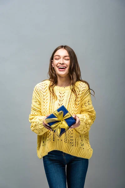 Glückliches Mädchen im gelben Pullover, das Geschenk isoliert auf grau haltend — Stockfoto