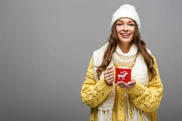 Happy girl in yellow sweater, scarf, hat holding mug of cocoa on grey — Stock Photo