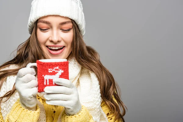 Happy girl in yellow sweater, scarf, hat and gloves holding mug of cocoa isolated on grey — Stock Photo