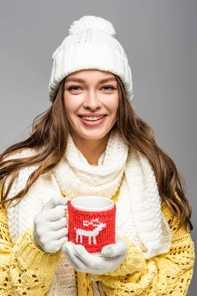 Fröhliches Mädchen in gelbem Pullover, Schal, Mütze und Handschuhen mit Kakaobecher in grau — Stockfoto