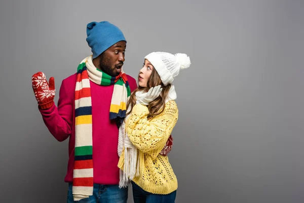 Sonriente interracial pareja en invierno traje abrazando en gris fondo - foto de stock