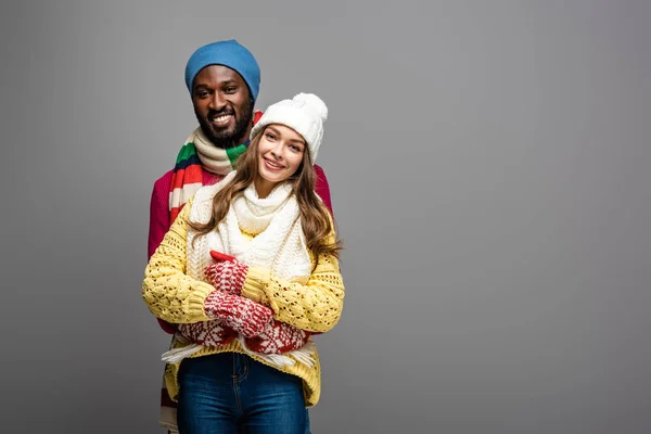 Feliz pareja interracial en invierno traje abrazando en gris fondo - foto de stock