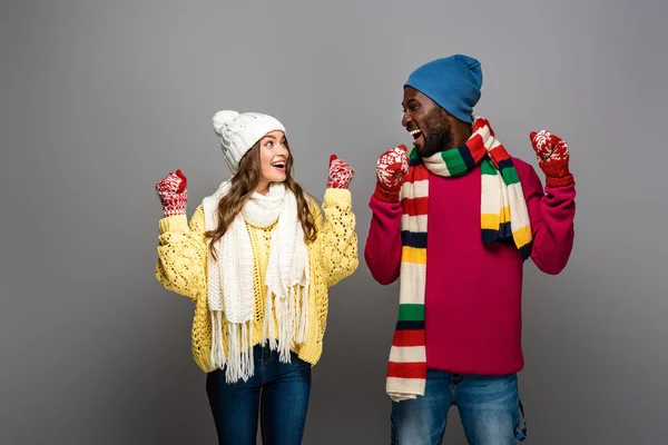 Feliz pareja interracial en invierno traje regocijo en gris fondo - foto de stock