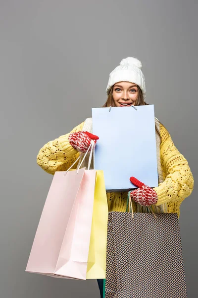 Glückliche Frau im winterlichen Outfit mit Einkaufstaschen auf grauem Hintergrund — Stockfoto
