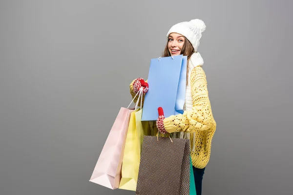 Glückliche Frau im winterlichen Outfit mit Einkaufstaschen auf grauem Hintergrund — Stockfoto