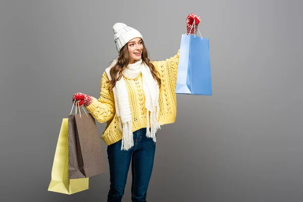 Femme heureuse en tenue d'hiver avec des sacs à provisions sur fond gris — Photo de stock