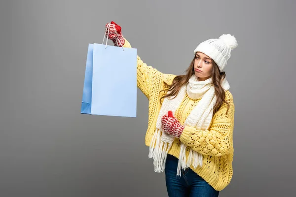 Грустная женщина в зимнем наряде с сумкой для покупок на сером фоне — стоковое фото