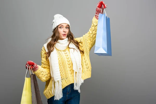 Mujer impactada en traje de invierno con bolsas de compras sobre fondo gris - foto de stock