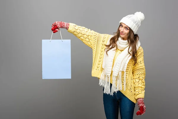 Усміхнена жінка в зимовому вбранні з сумкою для покупок на сірому фоні — стокове фото