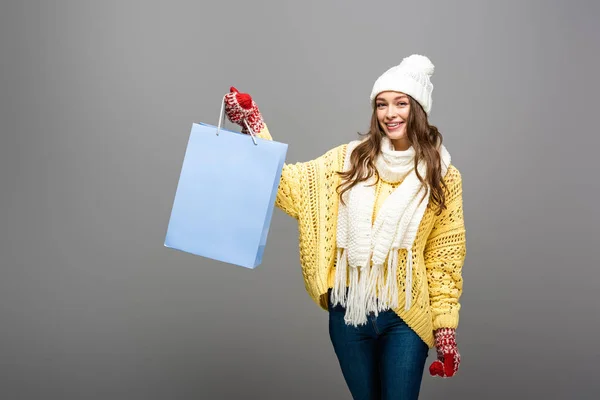 Mujer feliz en traje de invierno con bolsa de compras sobre fondo gris - foto de stock