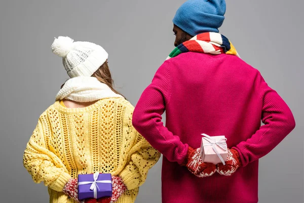 Visão traseira do casal interracial na exploração roupa de inverno apresenta isolado em cinza — Fotografia de Stock