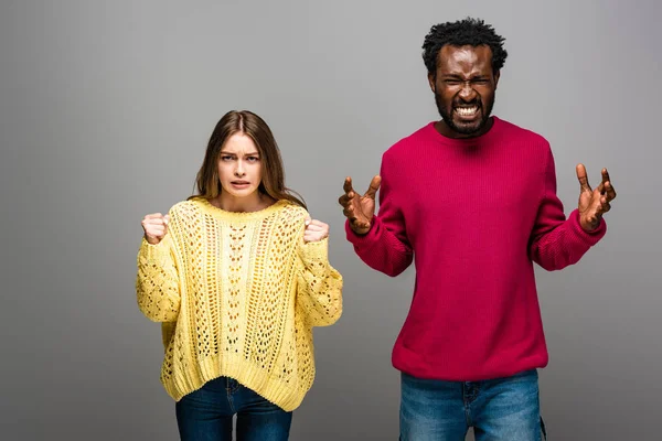 Angry interracial couple in knitted sweaters on grey background — Stock Photo