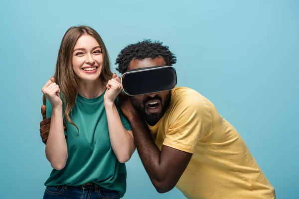 Excitada chica de pie cerca asustado afroamericano novio en vr auriculares aislados sobre fondo azul - foto de stock