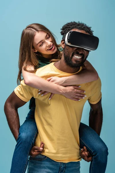 Menina feliz piggybacking no namorado americano africano no fone de ouvido vr isolado no azul — Fotografia de Stock