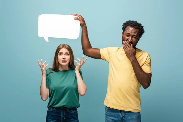 Afrikanisch-amerikanischer Mann hält Sprechblase über verwirrter Freundin auf blauem Hintergrund — Stockfoto