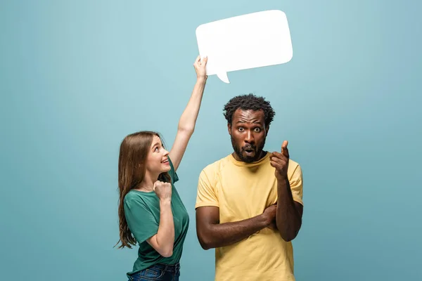 Girl holding speech bubble above african american man showing idea gesture on blue background — Stock Photo