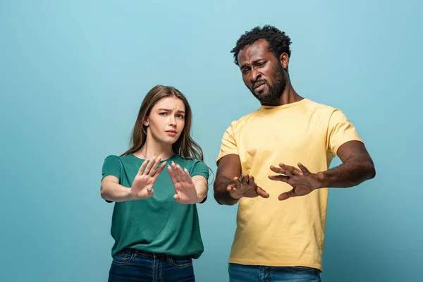 Confused interracial couple showing no gesture on blue background — Stock Photo