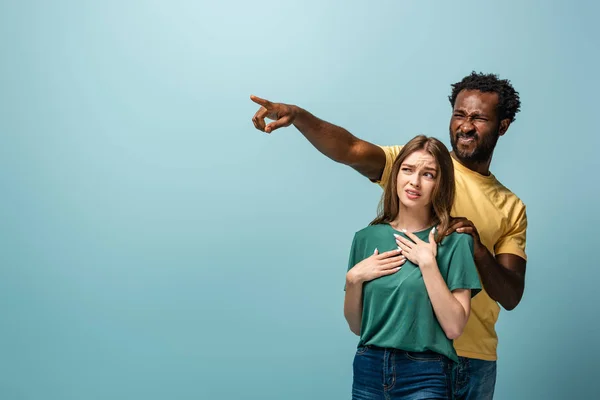 Confused interracial couple pointing with finger away on blue background — Stock Photo