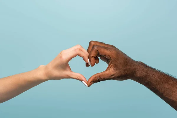 Recortado vista de interracial pareja mostrando corazón gesto aislado en azul - foto de stock