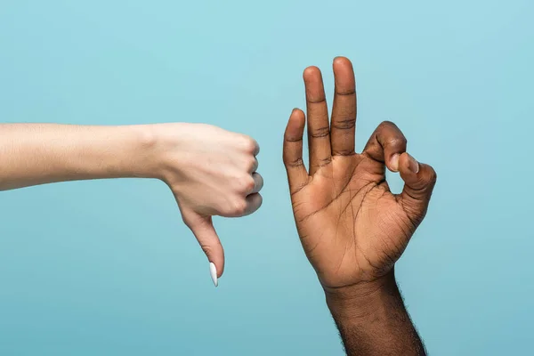 Cropped view of interracial couple showing thumb down and okay sign isolated on blue — Stock Photo