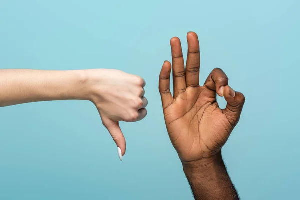 Recortado vista de interracial pareja mostrando pulgar hacia abajo y bien signo aislado en azul - foto de stock