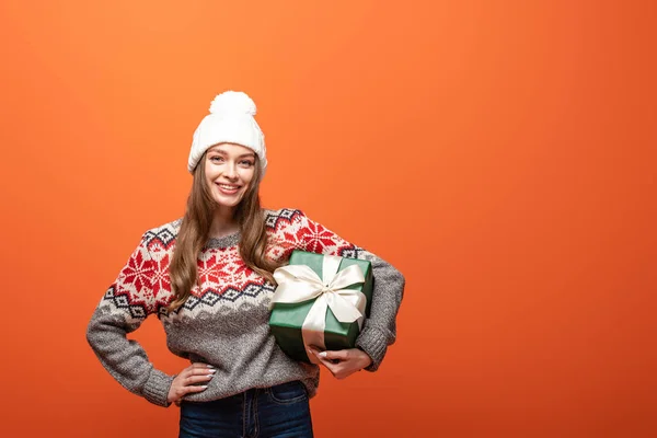 Happy girl in winter outfit holding present on orange background — Stock Photo