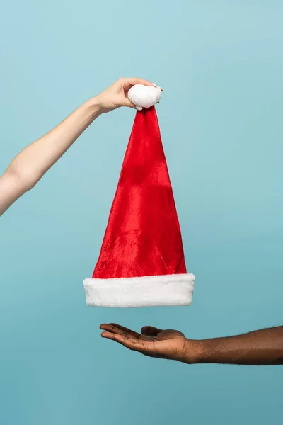 Vista ritagliata di coppia interrazziale tenendo Santa cappello isolato su sfondo blu — Foto stock