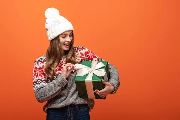 Menina feliz em roupa de inverno segurando presente no fundo laranja — Fotografia de Stock