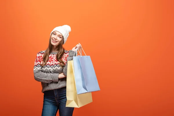 Chica feliz en traje de invierno sosteniendo bolsas de compras sobre fondo naranja - foto de stock