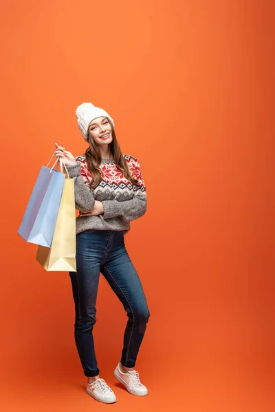 Счастливая девушка в зимнем наряде с сумками для покупок на оранжевом фоне — стоковое фото