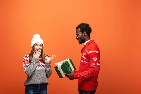 Africano americano uomo regalo di Natale per scioccato fidanzata su sfondo arancione — Foto stock
