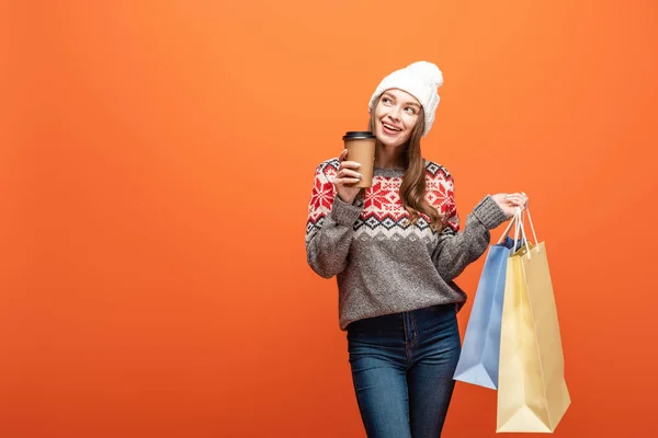 Menina feliz em roupa de inverno segurando sacos de compras e café para ir no fundo laranja — Fotografia de Stock