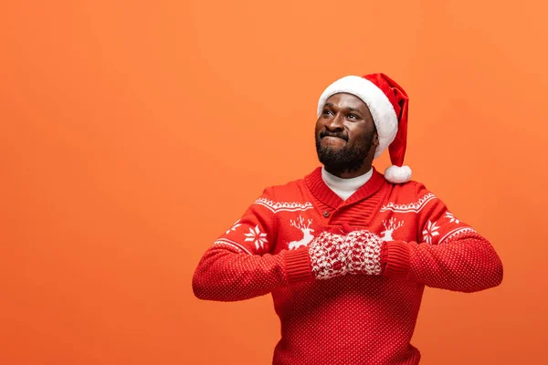 Homme afro-américain en colère dans santa chapeau, mitaines et pull de Noël sur fond orange — Photo de stock