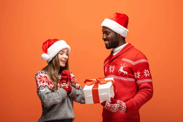 Afrikanisch-amerikanischer Mann verschenkt Weihnachtsgeschenk an glückliche Freundin auf orangefarbenem Hintergrund — Stockfoto
