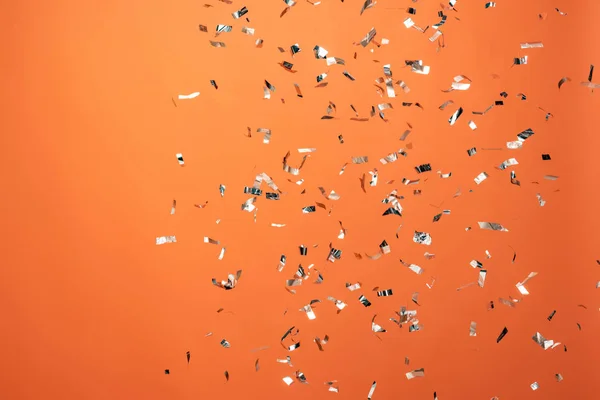 Shiny silver confetti on orange background — Stock Photo