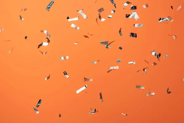 Shiny silver confetti on orange background — Stock Photo