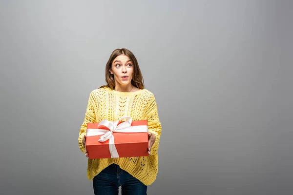 Excited happy woman in yellow sweater holding gift box on grey background — Stock Photo