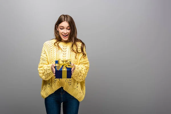 Excited happy woman in yellow sweater holding gift box on grey background — Stock Photo