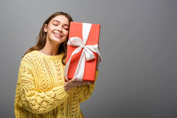 Pleased woman in yellow sweater holding gift box on grey background — Stock Photo