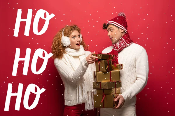 Happy couple in winter outfit holding christmas presents on red with ho ho ho illustration — Stock Photo