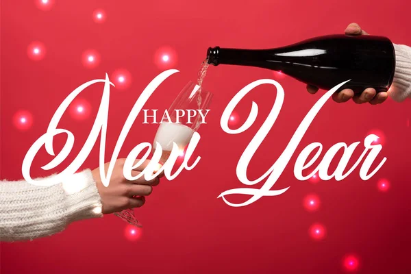 Cropped view of man pouring champagne from bottle into glasses on red with happy new year lettering — Stock Photo