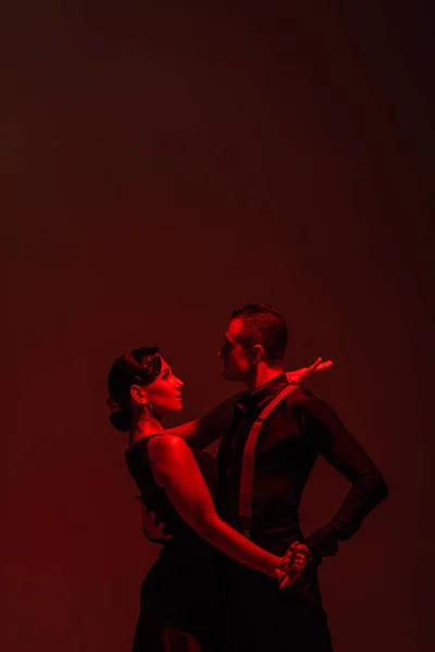 Sensual couple of dancers performing tango on dark background with red illumination — Stock Photo