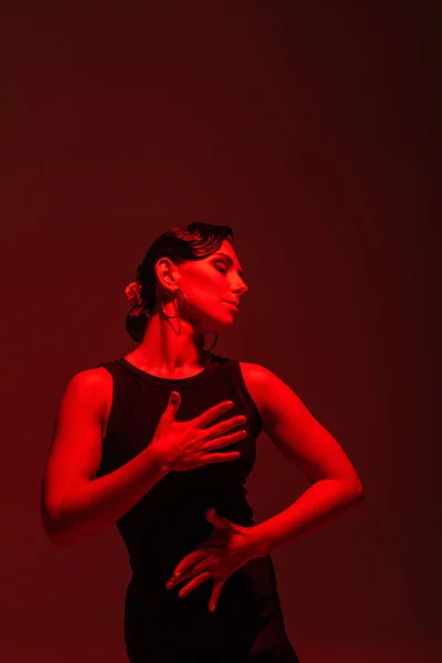 Sensual bailarina en vestido negro realizando tango sobre fondo oscuro con iluminación roja - foto de stock
