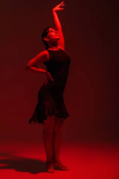 Elegante bailarina en vestido negro realizando tango sobre fondo oscuro con iluminación roja - foto de stock